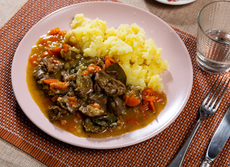 On light tablecloth there are portion of puree potatoes with large bits of fried chicken liver in thick vegetable gravy as main course. Dish decorated with parsley leaf
