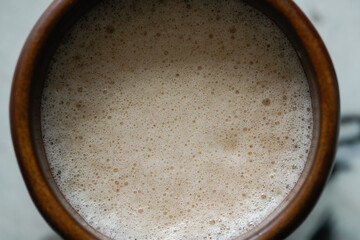 Captivating close-up of a frothy latte with delicate foam, nestled in a warm, rustic brown ceramic mug. 