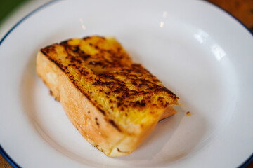 A piece of perfectly toasted garlic bread sits on a simple white plate. The toast is golden-brown and appears crispy. Golden-Brown Garlic Toast on a White Plate