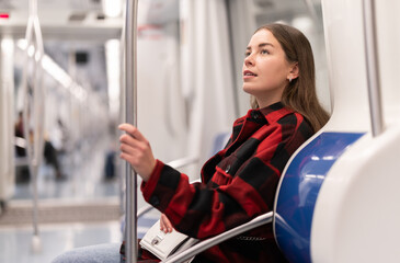 Young woman is sitting in the subway and looking at a map with stops and transfers. European woman...