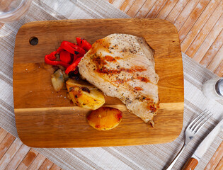 Delicious homemade grilled pork meat served on wooden board with baked potatoes and red pepper slices.