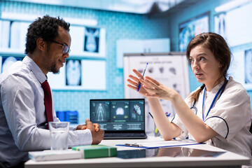 Woman physician reading x ray diagnostics for a patient in medical office, doing a test results...