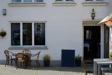 Fototapeta premium Outdoor seating area with tables and decorative plants near a restaurant entrance on a sunny day in a charming urban setting