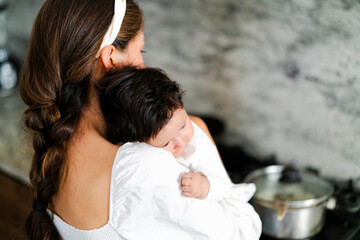Mother multitasking, cooking while holding her baby