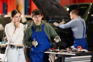 Auto mechanic checking young woman client car in car service center