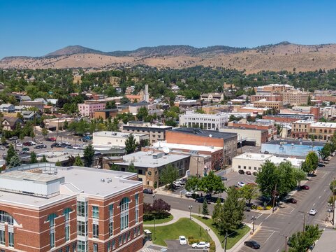 High-angle view of Klamath Falls town center, showcasing diverse architecture and ample parking. Sunny day, clear skies, and surrounding hills. Oregon, USA
