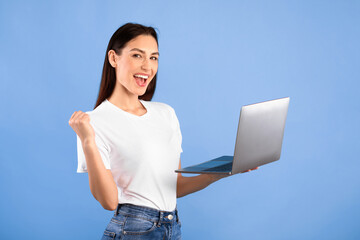 Yeah. Excited young woman celebrating online win, great deal or business success holding laptop...