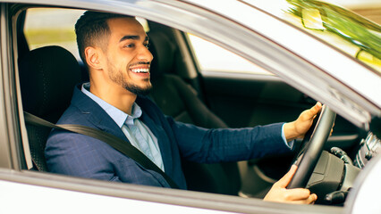 Joyful middle-eastern young businessman driving his new auto, going to office, shot from outside,...
