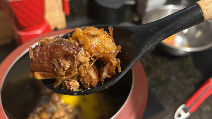 Chef holding spoon with pulled pork over pot in kitchen