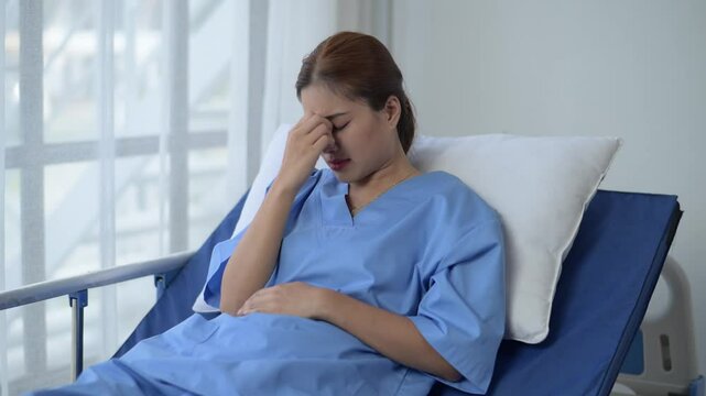 A woman in a blue hospital gown is laying on a bed with her head turned to the side