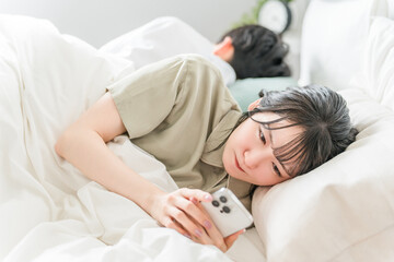 ベッドルームでスマホを見ながら泣く主婦・妻（夫婦喧嘩・モラハラ）
