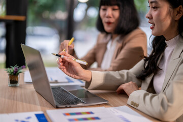Two women are sitting at a table with a laptop and papers in front of them
