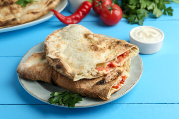Halves of tasty calzone with meat, cheese, tomato and sauce on light blue table, closeup