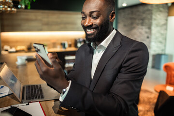 Smiling young black businessman using smartphone in modern office