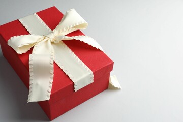 Beautiful gift box with beige bow on light grey background. Space for text