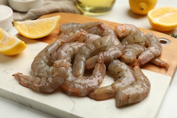Fresh raw shrimps and lemon wedges on white table, closeup