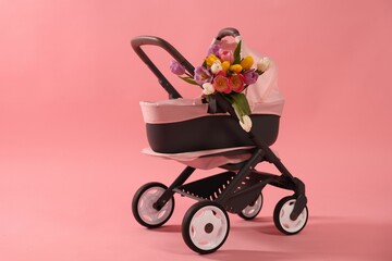 Stylish doll stroller and tulips on pink background. Kid's toy