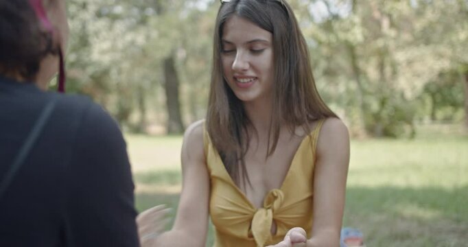 Friends having a picnic and playing a hand-clapping game in the park. They are laughing and enjoying their time together.