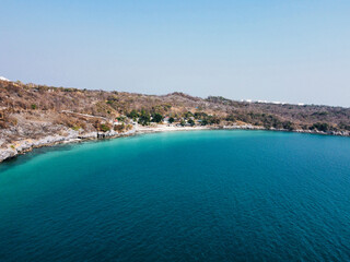 Fototapeta premium Aerial view of a tranquil coastline featuring clear turquoise waters and a rocky shoreline under a bright blue sky in Ko Sichang, Chonburi, Thailand