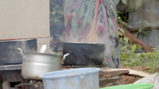 A woman stirs a large cooking pot over an open fire in Ethiopia, Africa.