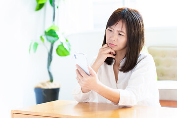 困った表情でスマートフォンを使う女性