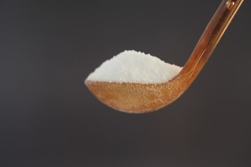 Spoonful of white sugar against dark background highlights texture