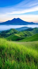 Fototapeta premium Experience the breathtaking beauty of this vibrant landscape, where rolling green hills meet a majestic mountain range shrouded in ethereal mist, creating a serene and captivating panorama that