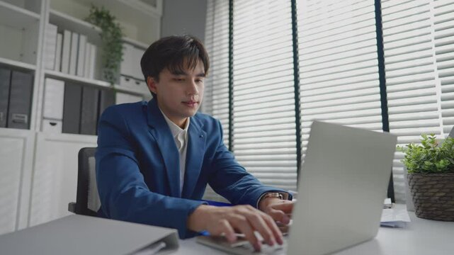 Asian businessman turning on laptop computer while working in office.