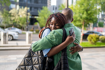 Smiling black wife laugh and hug husband tightly, emotional family reunion outdoors. Joy and love...