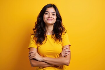 Obraz premium Confident Young Hispanic Woman in Yellow T-Shirt Smiling with Arms Crossed Against a Vibrant Yellow Background