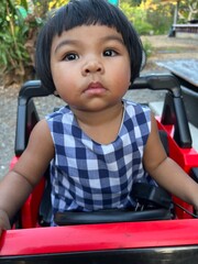 Portrait of cute little Asian girl playing inside a red car and looking at the camera in the park