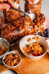 Hand serving with spoon healthy granola for breakfast with yogurt mixed with homemade granola and fruits mango, papaya and grapes.