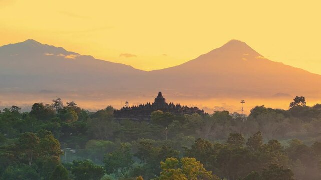 Aerial drone breathtaking view of the ancient ruins in the middle of forest with mountains and orange sunrise sky background . Borobudur Temple, Buddhist temple in Magelang, Central Java, Indonesia.