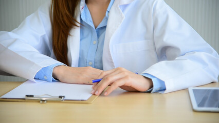 Fototapeta premium Close up hands of women doctor write prescription medical lab hospital. Crop asian women hand doctors working in medical clinic looking CAT scan xray film. Doctor with stethoscope writing on notepad