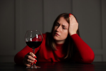 Alcohol addiction. Woman with glass of red wine at wooden table indoors, selective focus