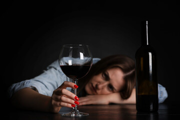 Alcohol addiction. Miserable woman with wine at table in dark, selective focus