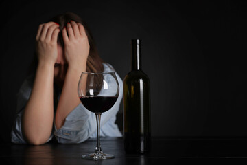 Alcohol addiction. Miserable woman with wine at table in dark. Space for text
