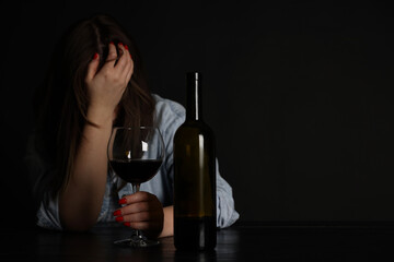 Alcohol addiction. Miserable woman with wine at table in dark. Space for text