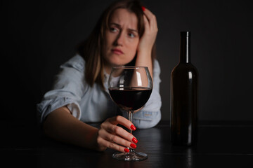Alcohol addiction. Miserable woman with wine at table in dark, selective focus