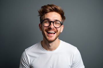 Obraz premium Cheerful Young Adult Male with Glasses Smiling Against a Neutral Gray Background, Capturing a Moment of Joy and Confidence in a Casual Setting