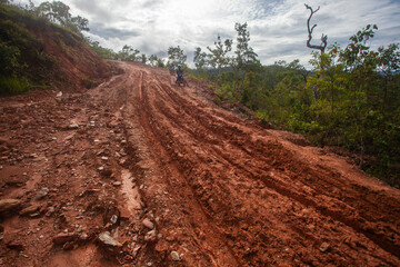Unidentified motorcyclists in Aileu, Timor Leste, struggle to navigate a muddy dirt road. Road...