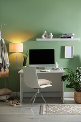 Home office. Comfortable workplace with desk, computer and lamp near light green wall in room
