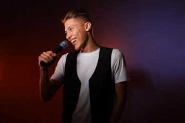 Talented young man singing on dark background with color light