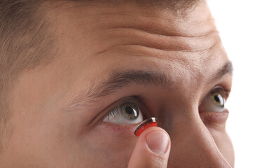 Man putting color contact lens in his eye on light background, closeup