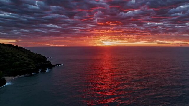 A dramatic sunrise over a vast ocean, the sky painted in fiery hues, reflecting on the water, surrounded by wild nature.
