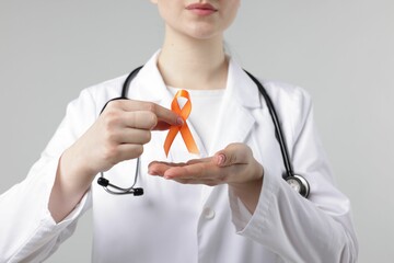 Multiple Sclerosis awareness. Doctor holding orange ribbon on light grey background, closeup