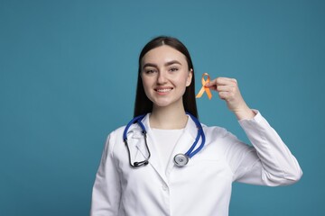 Multiple Sclerosis awareness. Happy doctor holding orange ribbon on light blue background