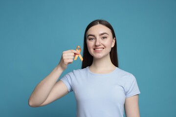 Multiple Sclerosis awareness. Happy young woman holding orange ribbon on light blue background