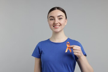 Multiple Sclerosis awareness. Happy young woman holding orange ribbon on light grey background