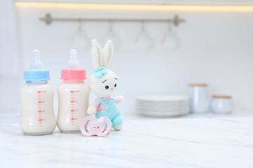Feeding bottles with baby formula, pacifier and toy bunny on white table indoors. Space for text